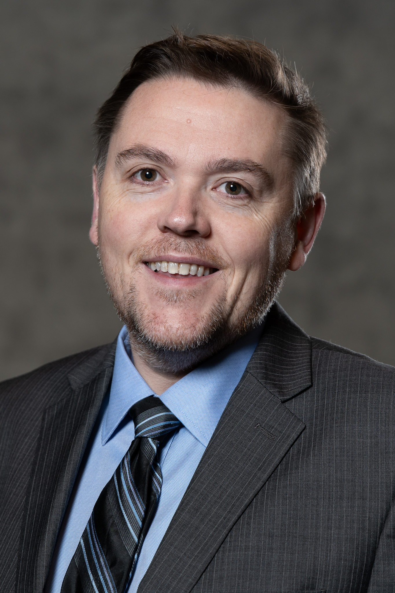 Conor Lennon smiling in a grey suit, blue shirt, and tie